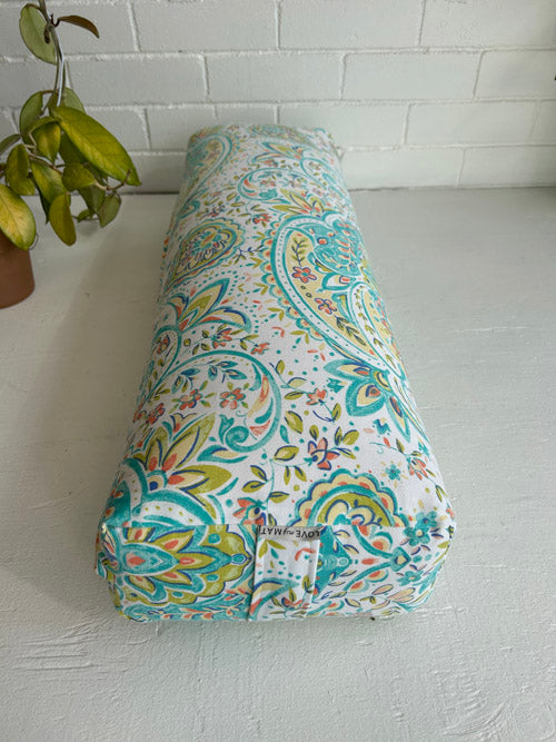 Decorative long yoga bolster with floral pattern on a white surface.