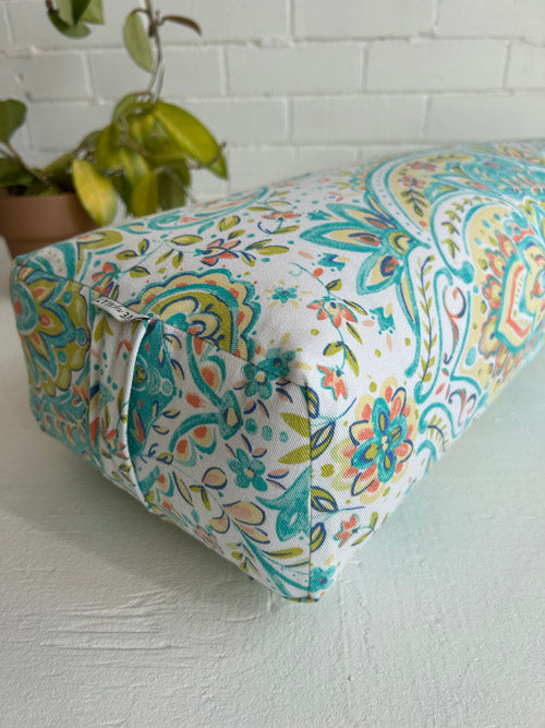 Close up of colourful fabric yoga bolster on a white surface with a plant in the background