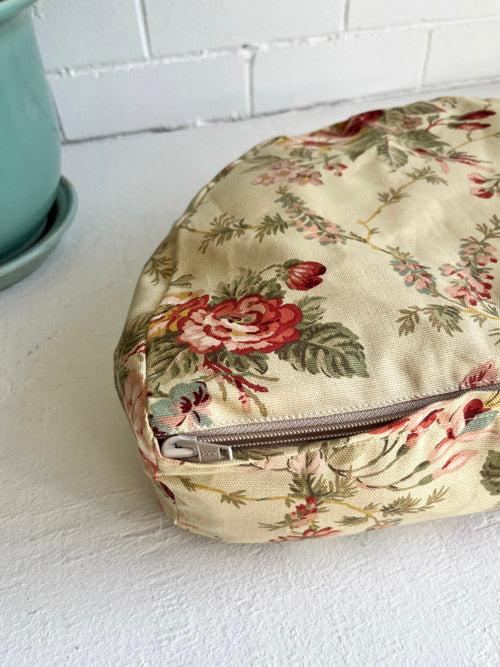Floral-patterned zippered meditation floor cushion on a white surface with a light blue pot in the background