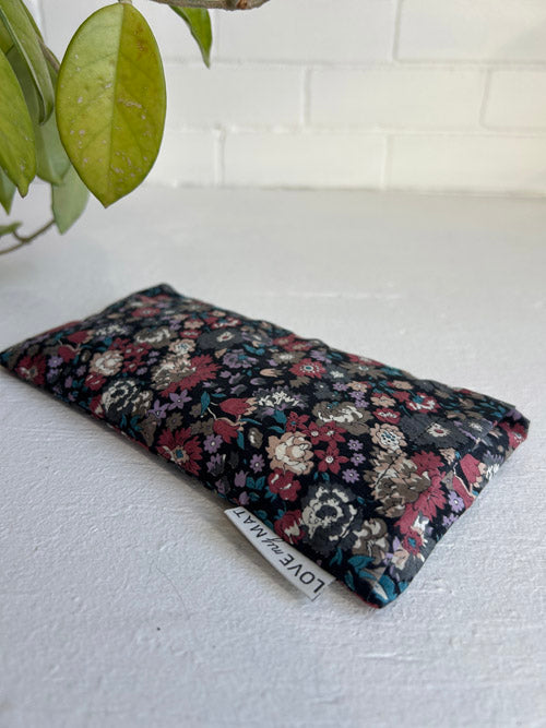 Floral-patterned eye pillow on a white surface with a plant in the corner