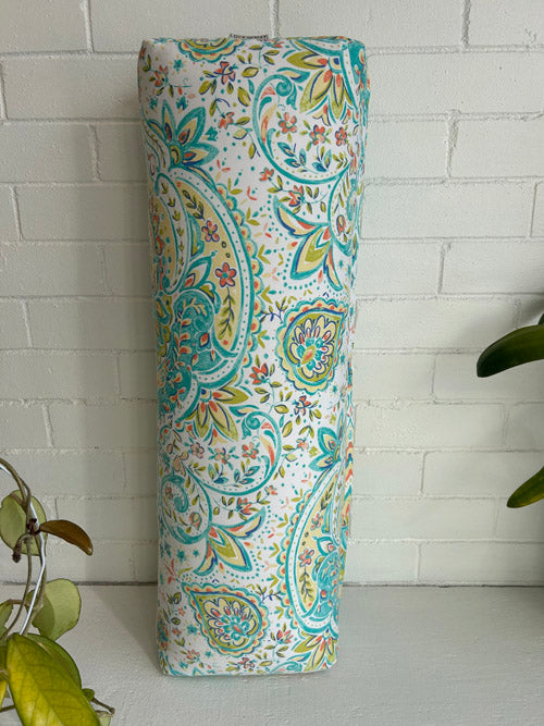 Decorative long yoga bolster with paisley pattern against a white brick wall