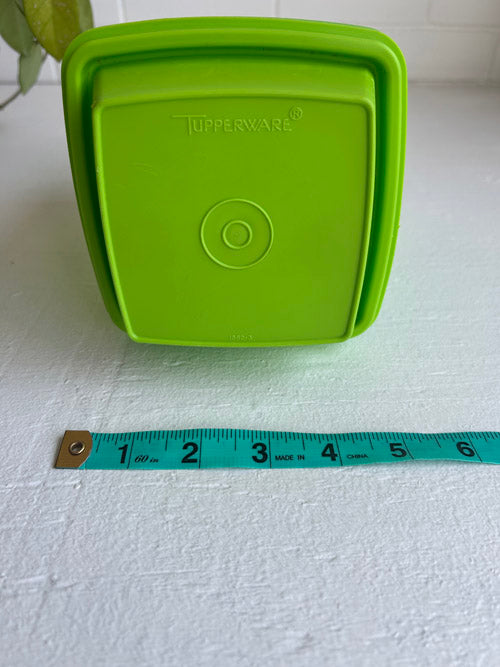 Green Tupperware container lid with a measuring tape for scale on a white background