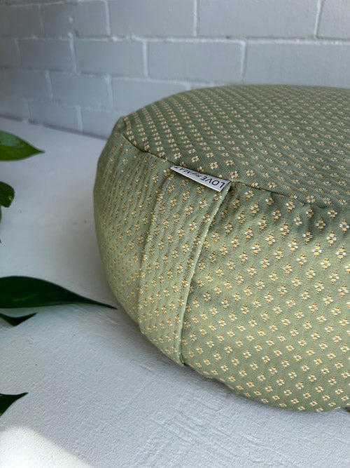 Green patterned meditation floor cushion on a white surface with a blurred background
