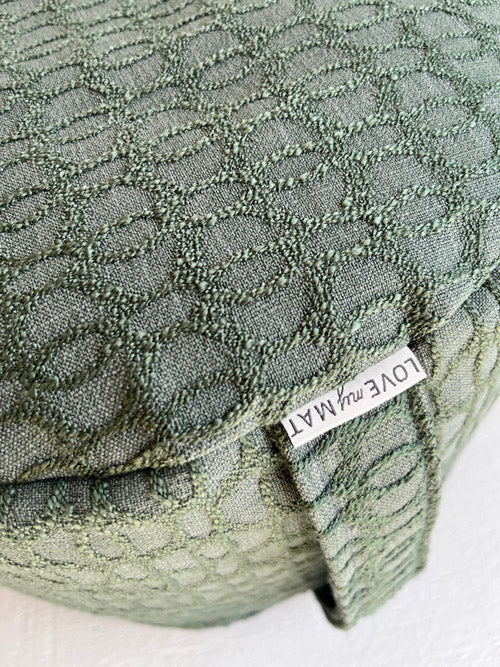Textured green fabric meditation floor cushion with a brand label on a white background