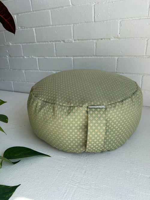 Green patterned zafu cushion on a white surface with a white brick wall background