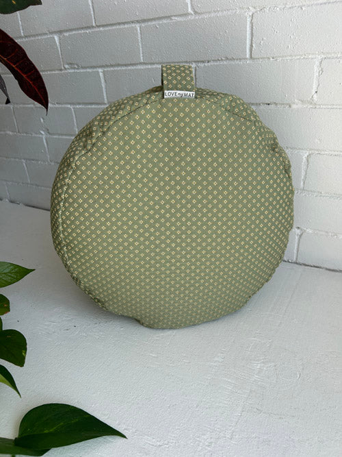Round green floor cushion with a pattern on a white surface with a white brick wall background