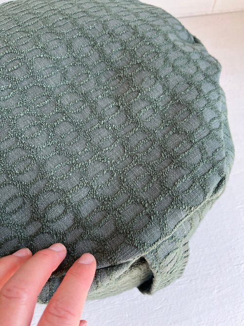 Textured green fabric with a hand touching it on a light background