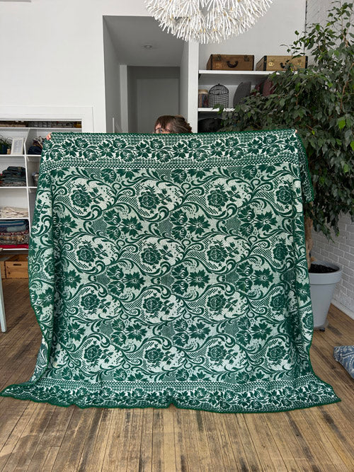 Green patterned blanket draped over a chair in a room with plants and shelves.