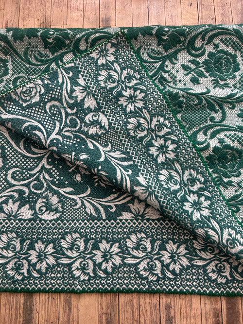 Green wool blanket with white floral patterns on a wooden surface