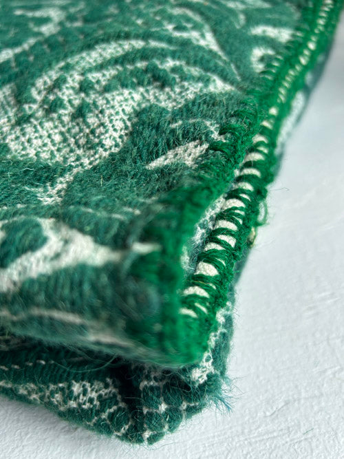 Close-up of green wool blanket with white pattern on a white background