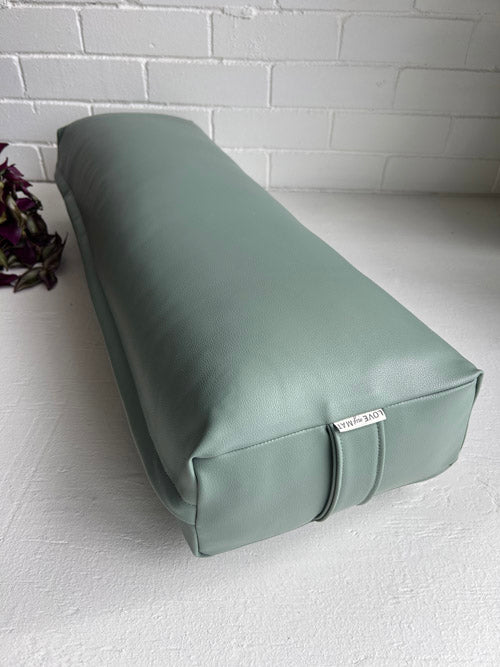 Green rectangular yoga bolster on a white surface with a white brick wall background