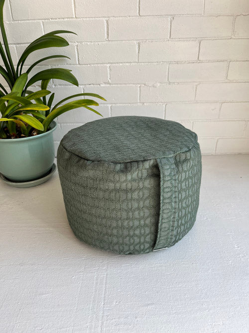 Green textured tall meditation floor cushion on a white surface with a plant in the background