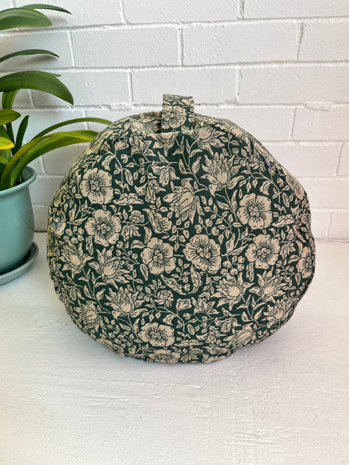 Floral-patterned meditation floor cushion on its side on a white surface with a plant in the background