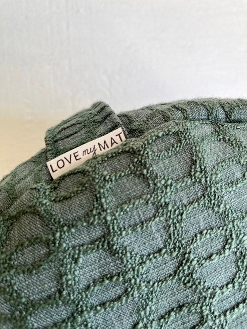 Close up of a green textured meditation cushion with 'LOVE my MAT' label on a white background