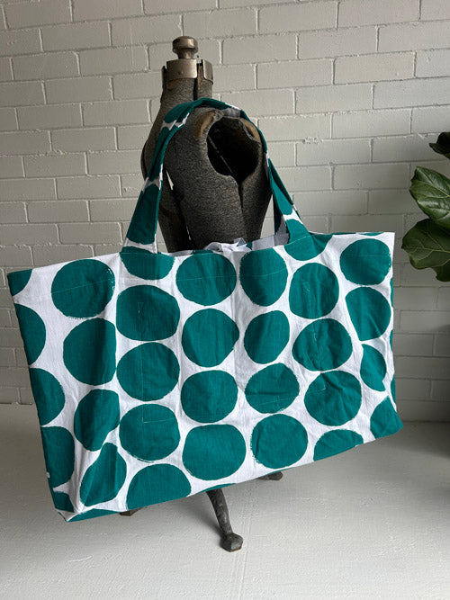 Large tote bag with teal polka dots on a mannequin against a white brick wall.