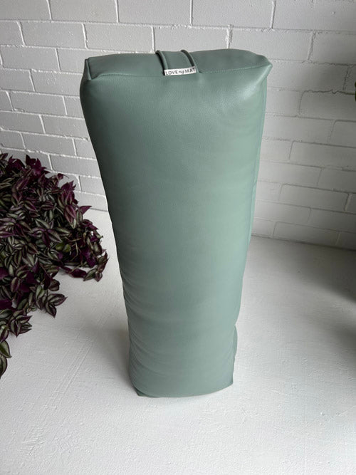 Green yoga long bolster with a label on a white surface against a white brick wall.