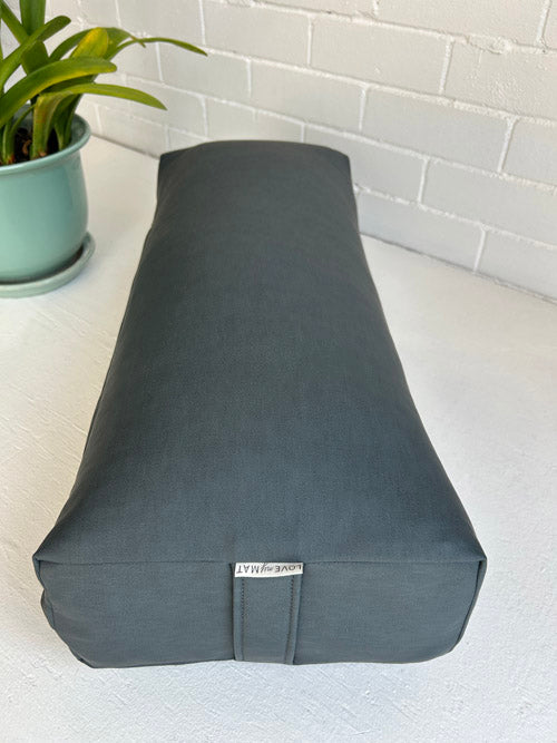 Gray yoga bolster on a white surface with a plant in the background