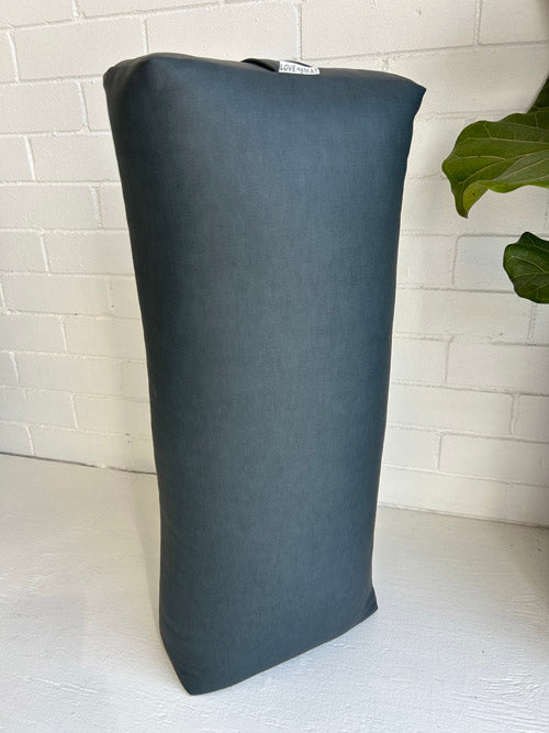 Dark gray Traditional yoga bolster on a white surface with a light-colored brick wall background