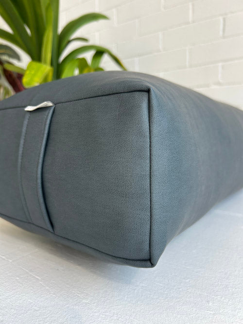 Gray traditional yoga bolster on a white surface with a plant in the background