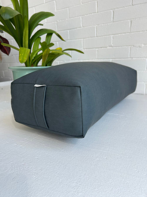 Gray yoga bolster on a white surface with a plant in the background