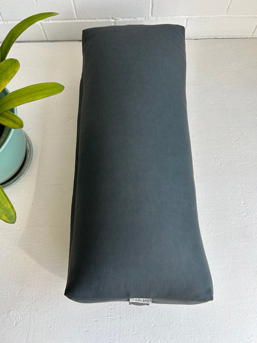 Grey blue vinyl yoga bolster on a light surface with a plant in the corner