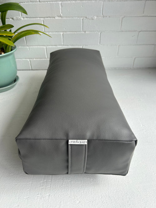 Gray vegan leather traditional yoga bolster with a plant on a white surface