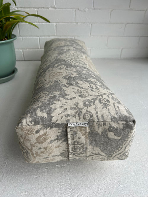 Fabric Long yoga Bolster with floral pattern on a white surface with a plant in the background