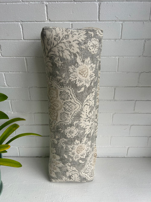 Decorative yoga bolster with floral pattern against a white brick wall.