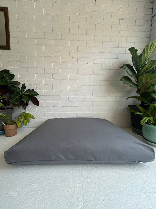 Gray cushion on a white surface with plants in the background