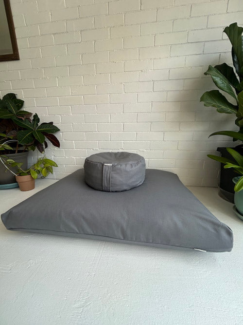 Gray cushion and pillow on a white surface with a white brick wall background