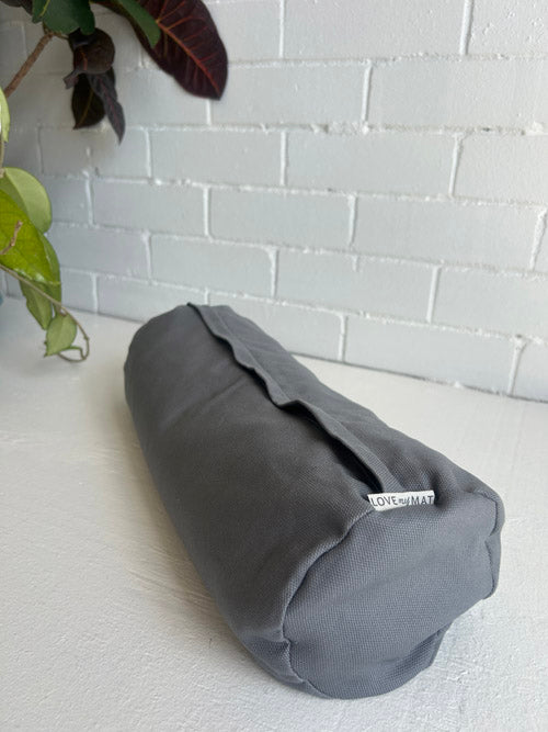 Gray cylindrical yoga bolster on a white surface with a light gray brick wall in the background