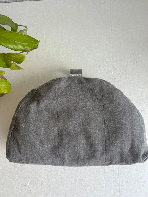 Gray fabric pouch on a white surface with a plant in the corner