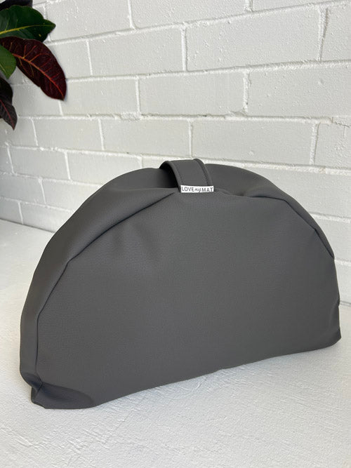 Gray vinyl meditation cushion with a brand label on a white surface and light gray brick wall background