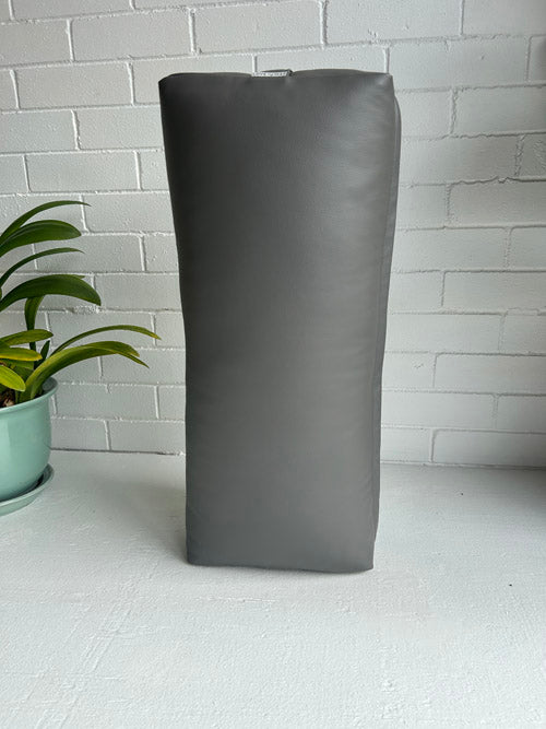 Grey vinyl yoga bolster against a white brick wall with a plant to the left.