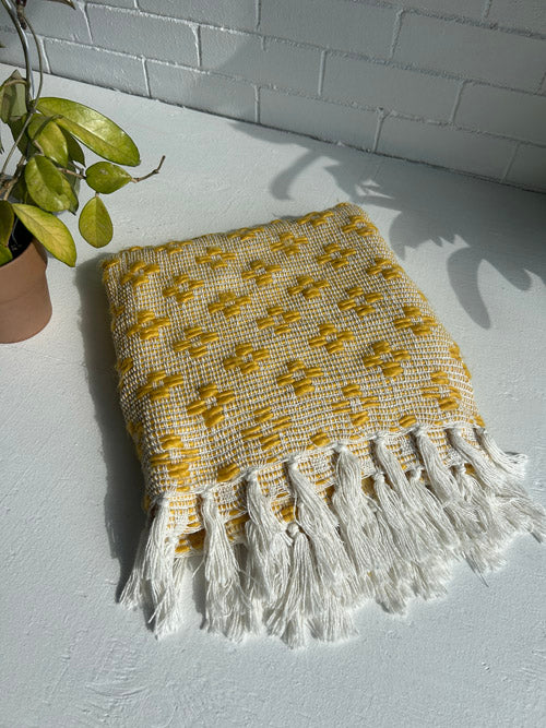 Yellow and white woven blanket with fringes on a white surface.