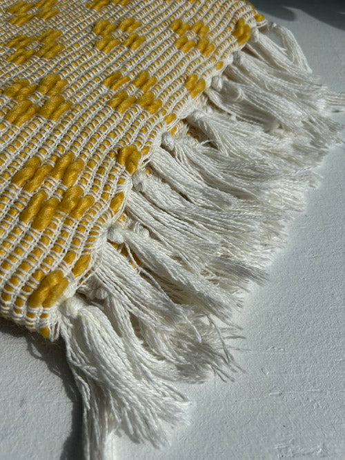 Textile with yellow pattern and white fringe on a light gray background