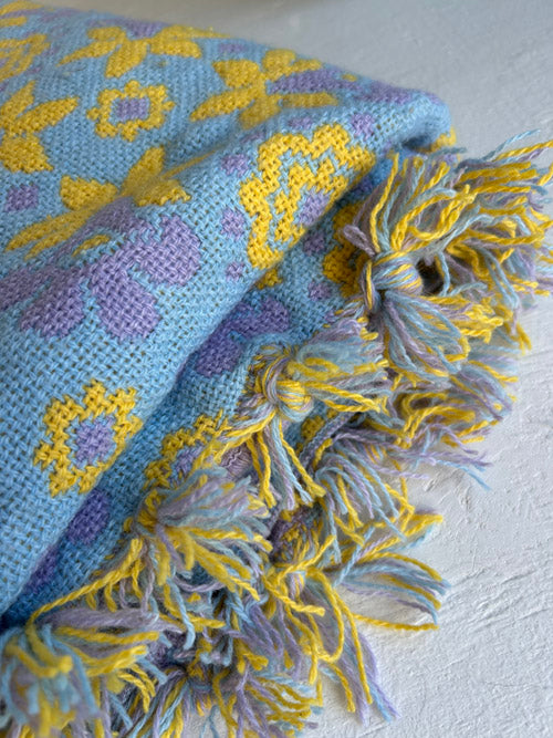 Knitted blanket with blue and purple pattern and yellow tassels on a light gray background