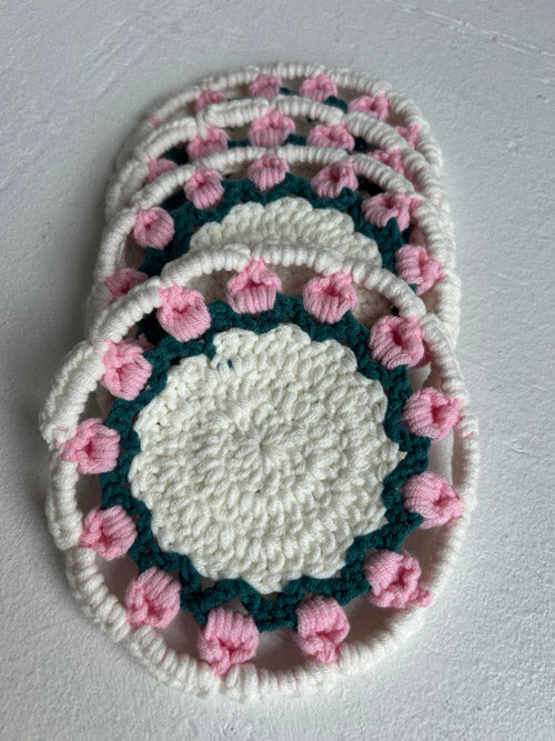 Set of crocheted coasters with pink flower patterns on a light gray background