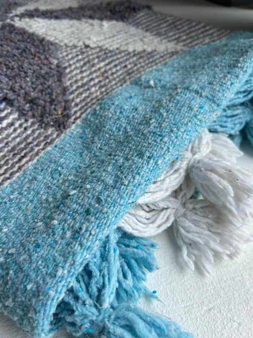 Close-up of a blue and gray checkered blanket with tassels on a white surface