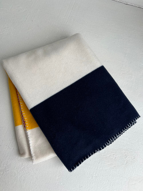 Two color-blocked blanket, one white and navy, the other yellow and white, on a white surface.