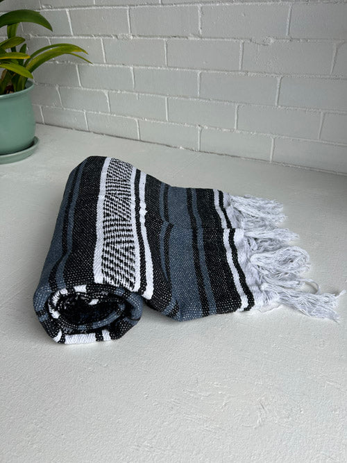 Rolled-up Blue,black and white striped towel with tassels on a light gray surface.