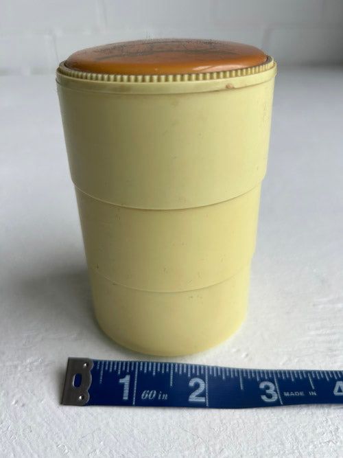 Beige cylindrical container with a brown lid on a white background, measured by a blue ruler.