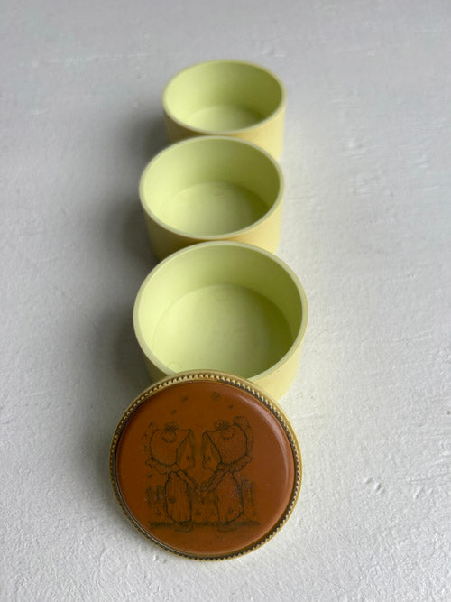 Three yellow cylindrical containers with a brown lid featuring a design on a gray background