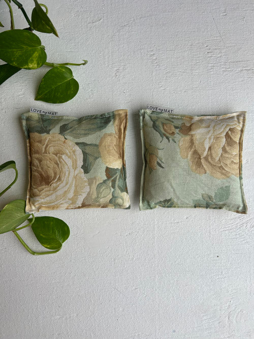 Two floral-patterned fabric yoga knee pillows  on a white surface with green leaves.