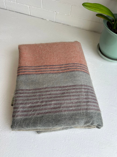 Folded blanket with pink and gray stripes on a white surface with a plant in the background