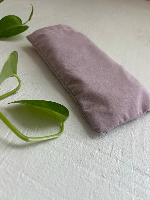 Purple eye pillow on a white surface with green leaves