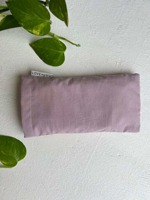 Purple eye pillow on a white surface with green leaves