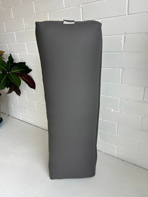 Gray long yoga bolster pillow on a white surface with a white brick wall background
