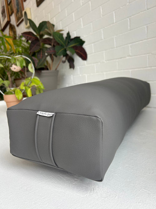 Gray vinyl yoga bolster on a white surface with plants in the background
