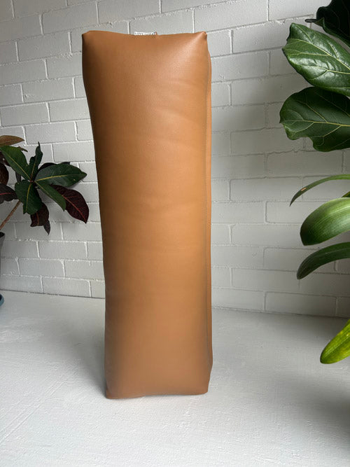 Long brown vinyl bolster for yoga on a white surface with plants in the background